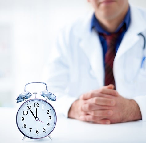 A clock sits on a desk in front of a doctor.